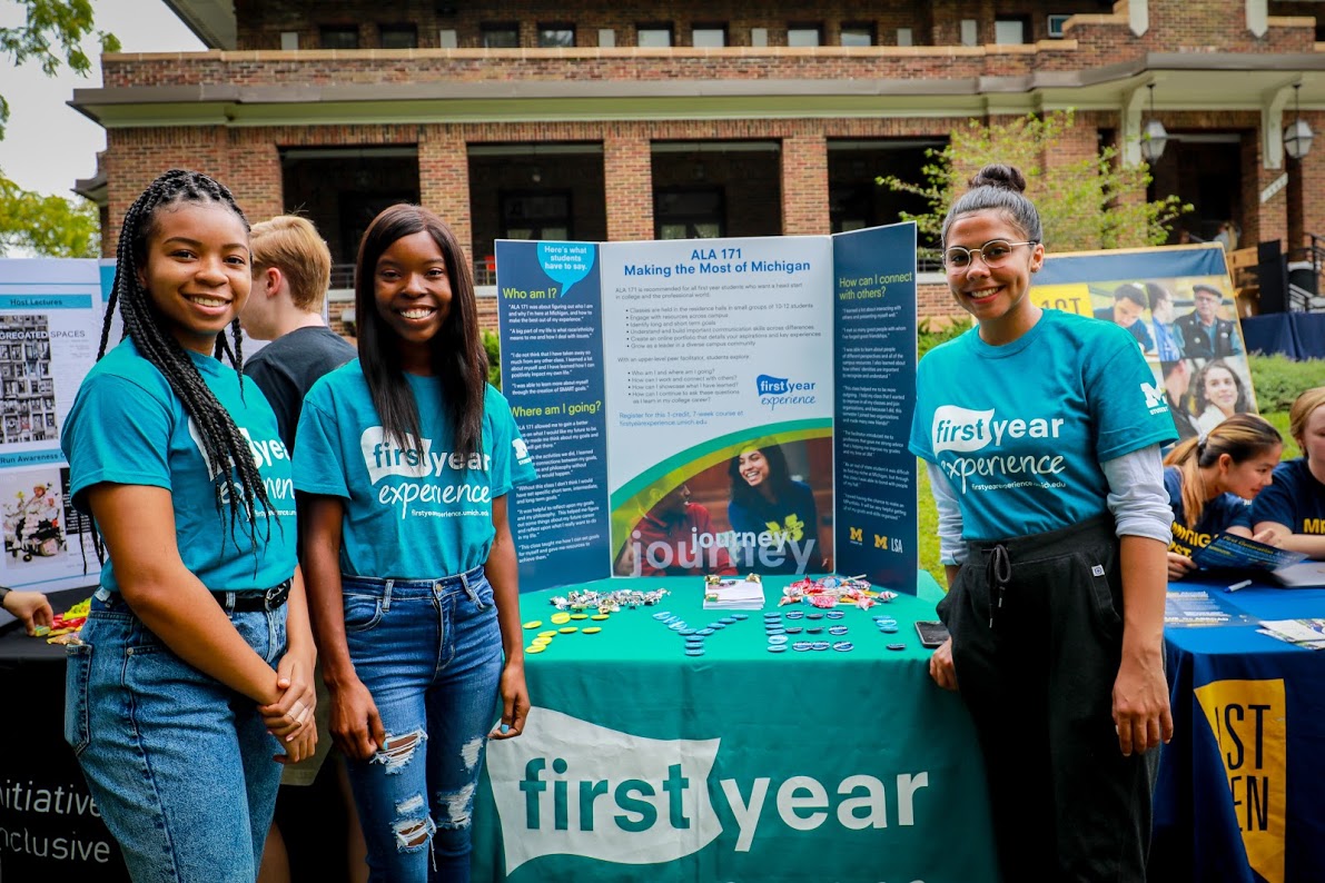 3 Students in front of 1443 Washtenaw at the First Year Experience info table